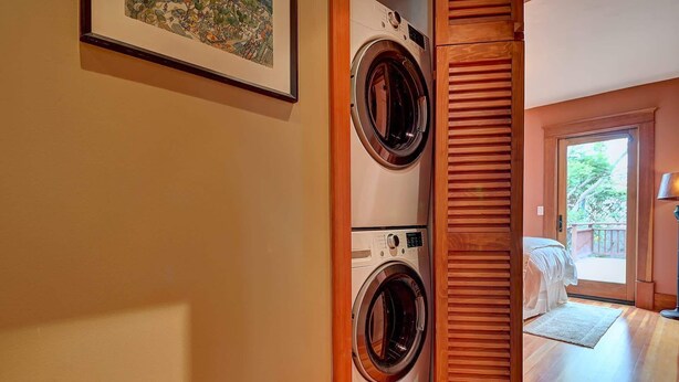 A laundry room with two stacked front-loading washers and dryers, wooden paneling, and a framed picture on the wall. - Moden Craftsman • Pet Friendly • Sleeps 6 (Long Beach)