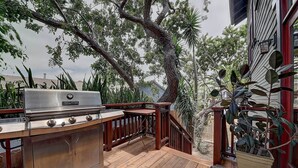 An outdoor deck with a stainless steel grill, wooden railing, and potted plants. - Moden Craftsman • Pet Friendly • Sleeps 6 (Long Beach)