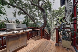 An outdoor deck with a stainless steel grill, wooden railing, and potted plants. - Moden Craftsman • Pet Friendly • Sleeps 6 (Long Beach)