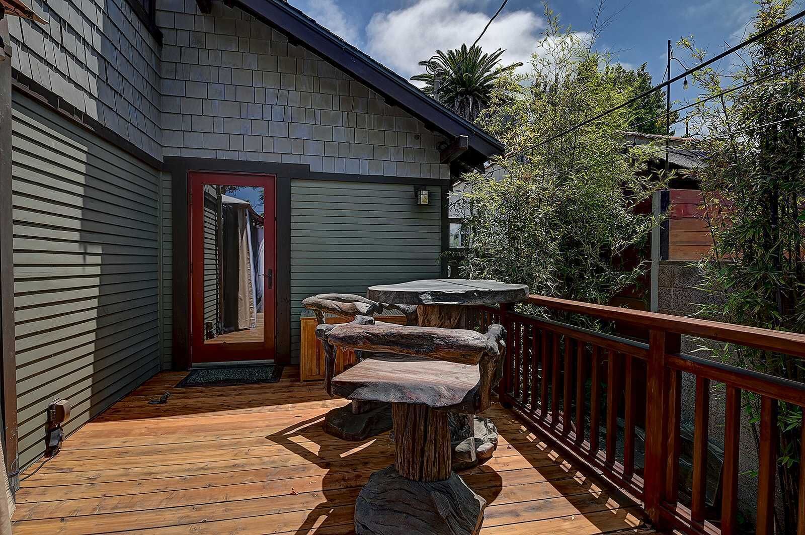 A wooden deck with a stone bench and a red door.