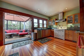 A compact kitchen with wooden cabinets, a built-in stove, and a dining area with a red sofa. - Moden Craftsman • Pet Friendly • Sleeps 6 (Long Beach)