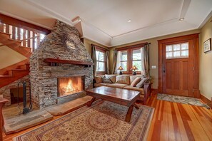 A living room with a stone fireplace, wooden staircase, and a sofa with cushions. - Moden Craftsman • Pet Friendly • Sleeps 6 (Long Beach)