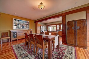 Un coin repas avec une table en bois, des chaises et un tapis. Il y a un tableau au mur et un meuble avec des tiroirs.