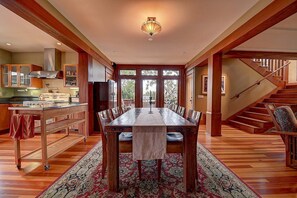 A spacious dining area with a long wooden table, surrounded by chairs, and a kitchen with wooden cabinets and appliances. - Moden Craftsman • Pet Friendly • Sleeps 6 (Long Beach)