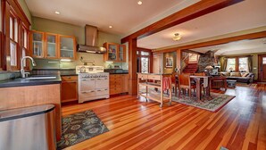 A spacious kitchen with wooden cabinets, a large stove, and a dining area with a staircase leading to another level. - Moden Craftsman • Pet Friendly • Sleeps 6 (Long Beach)