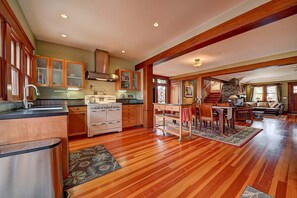 A spacious kitchen with wooden cabinets, a large stove, and a dining area with a staircase leading to another level. - Moden Craftsman • Pet Friendly • Sleeps 6 (Long Beach)