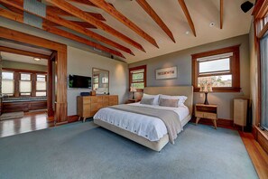 A bedroom with a large bed, wooden beams on the ceiling, a dresser, a television, and a window with a view. - Moden Craftsman • Pet Friendly • Sleeps 6 (Long Beach)