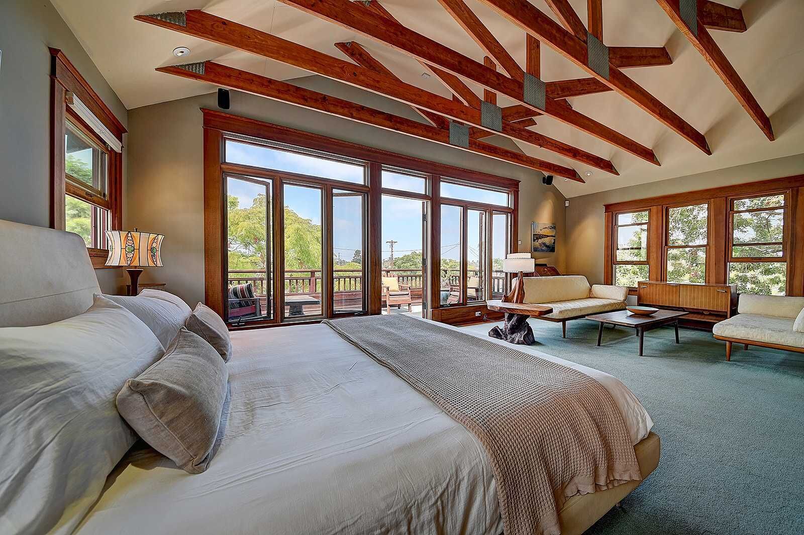 A spacious bedroom with a large bed, a sofa, and a dining table. There are large windows and a balcony.