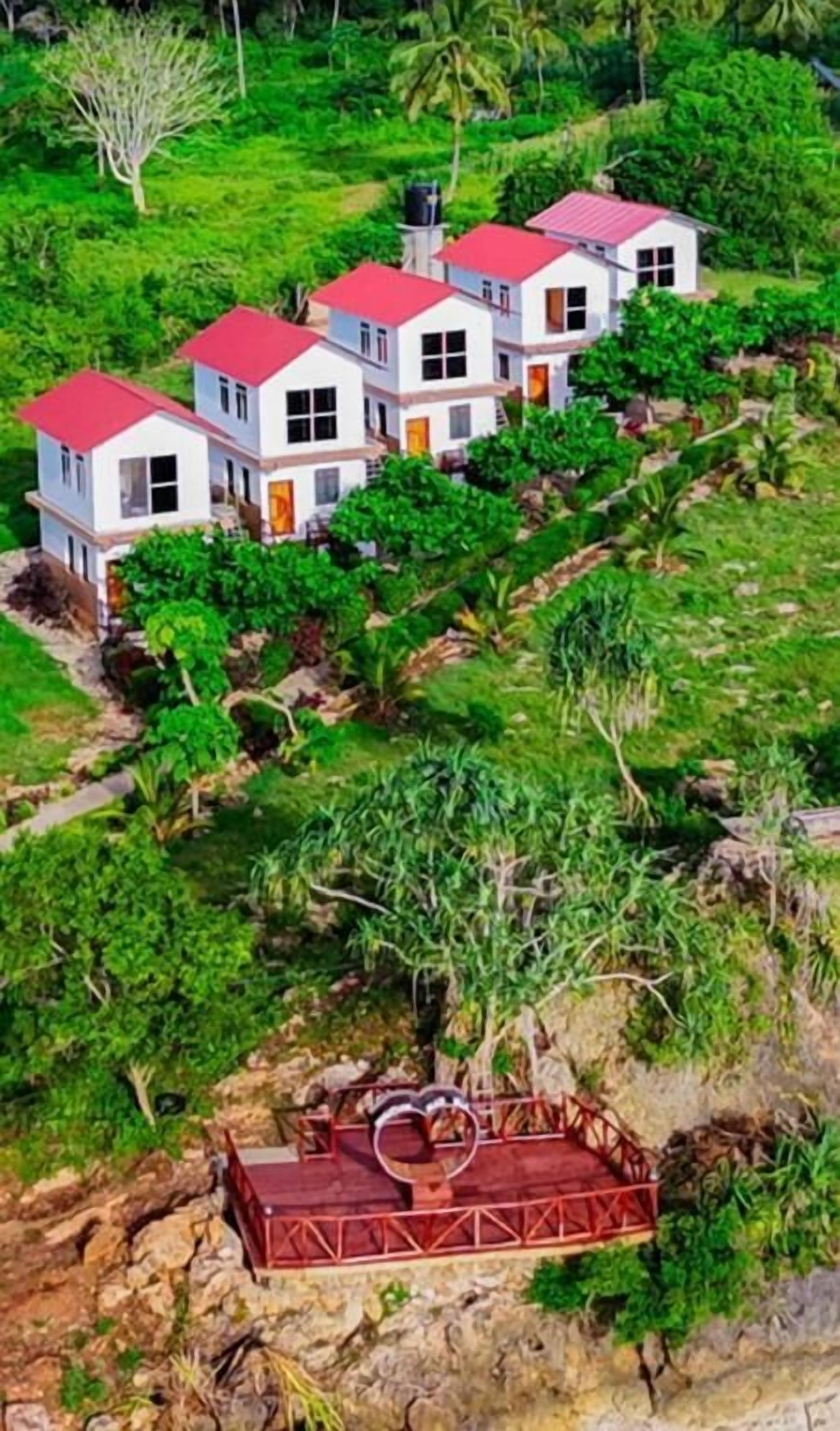 Un edificio de varios pisos con techo rojo, rodeado de exuberante vegetación y terreno rocoso.