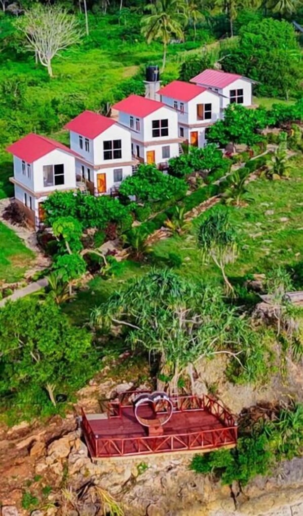 A multi-story building with a red roof, surrounded by lush greenery and a rocky terrain.