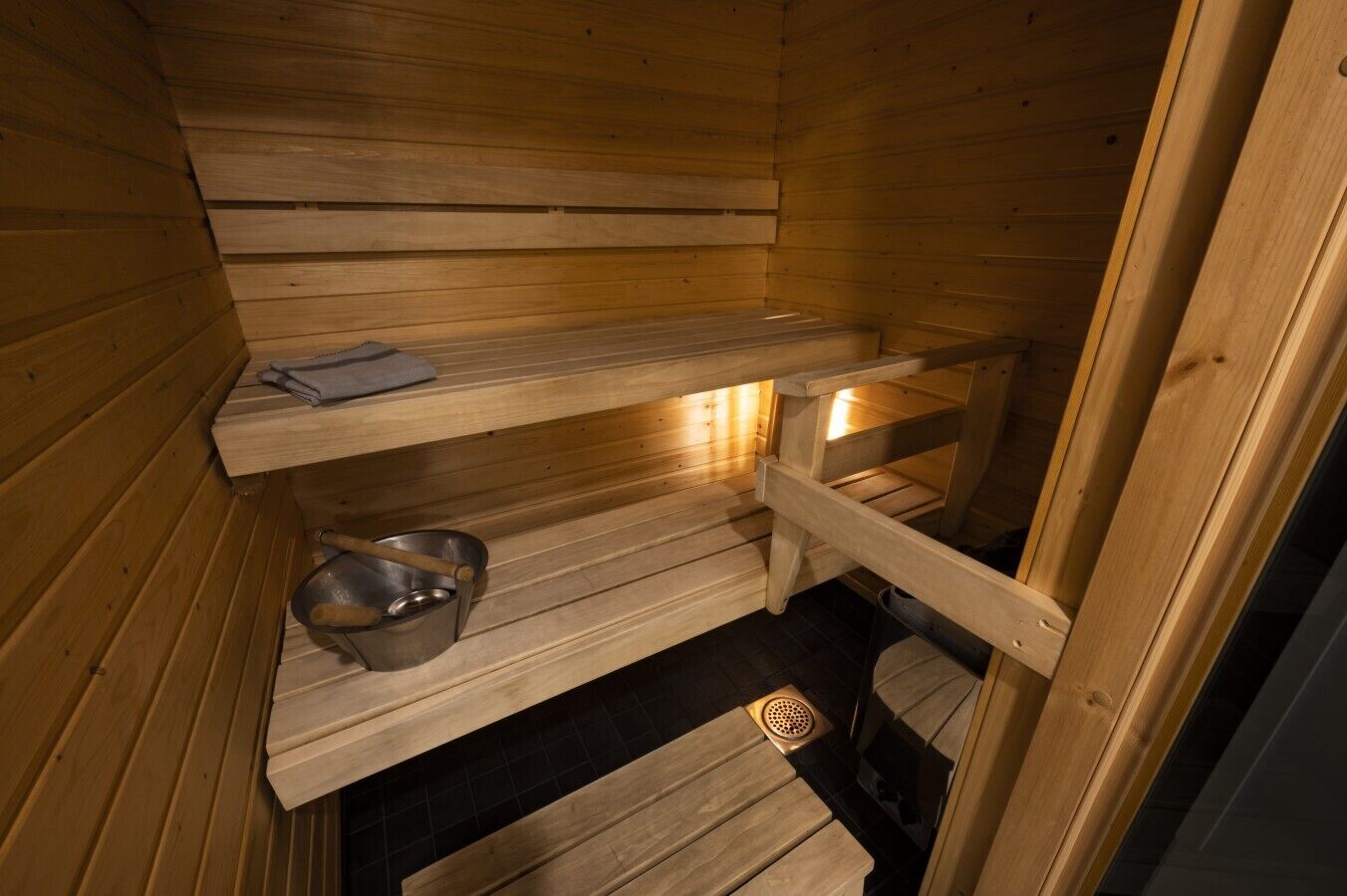 Eine Holzsauna mit Bänken, einer Ablage für Handtücher und einem Metall-Eimer.
