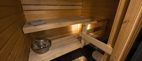 A wooden sauna with benches, a shelf with towels, and a metal bucket.
