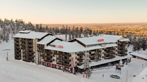 A multi-story hotel with a ski rental sign, surrounded by snow-covered trees and a flat landscape in the background. - Ruka Ski Chalets (60m²) with balcony and WiFi (Kuusamo)