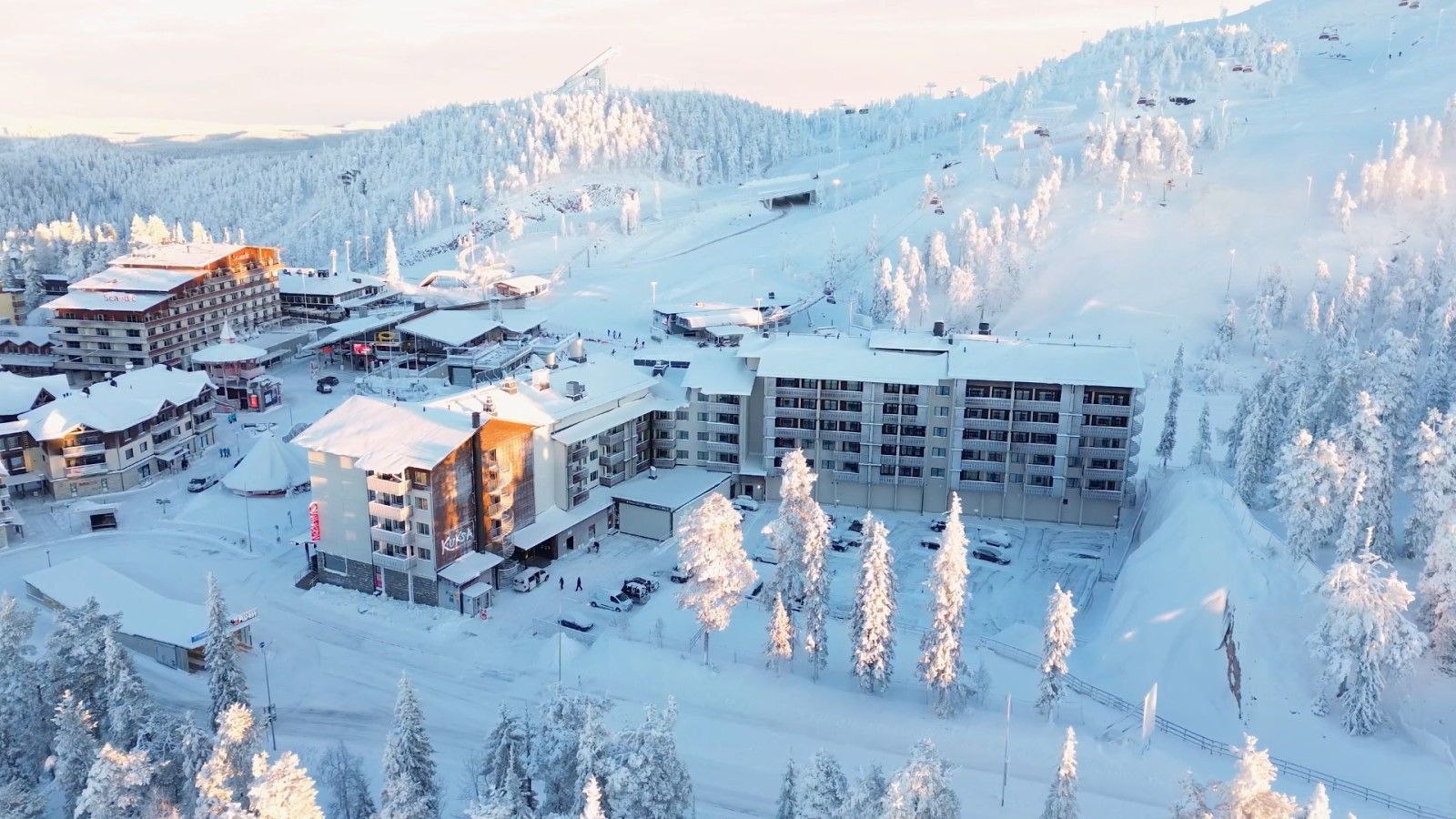 A snow-covered ski resort with multiple buildings, including a hotel and a ski lift area.