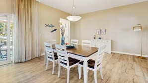 A dining area with a wooden table, white chairs, a hanging light fixture, and a view of the outdoors. - 3111 Poolside Villa, New Listing Deal ~ Book Sept 7th Today!  Pools, Bar, Gym (Destin)