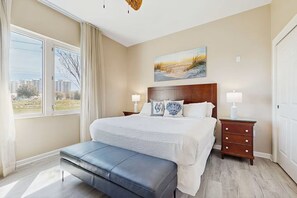 A hotel room with a large bed, two bedside tables, a bench, a painting above the bed, and a view of buildings through the window. - 3111 Poolside Villa, Family Fun ~ Book Oct 22nd ~ Pools Bar Gym Dining Hot Tub (Destin)