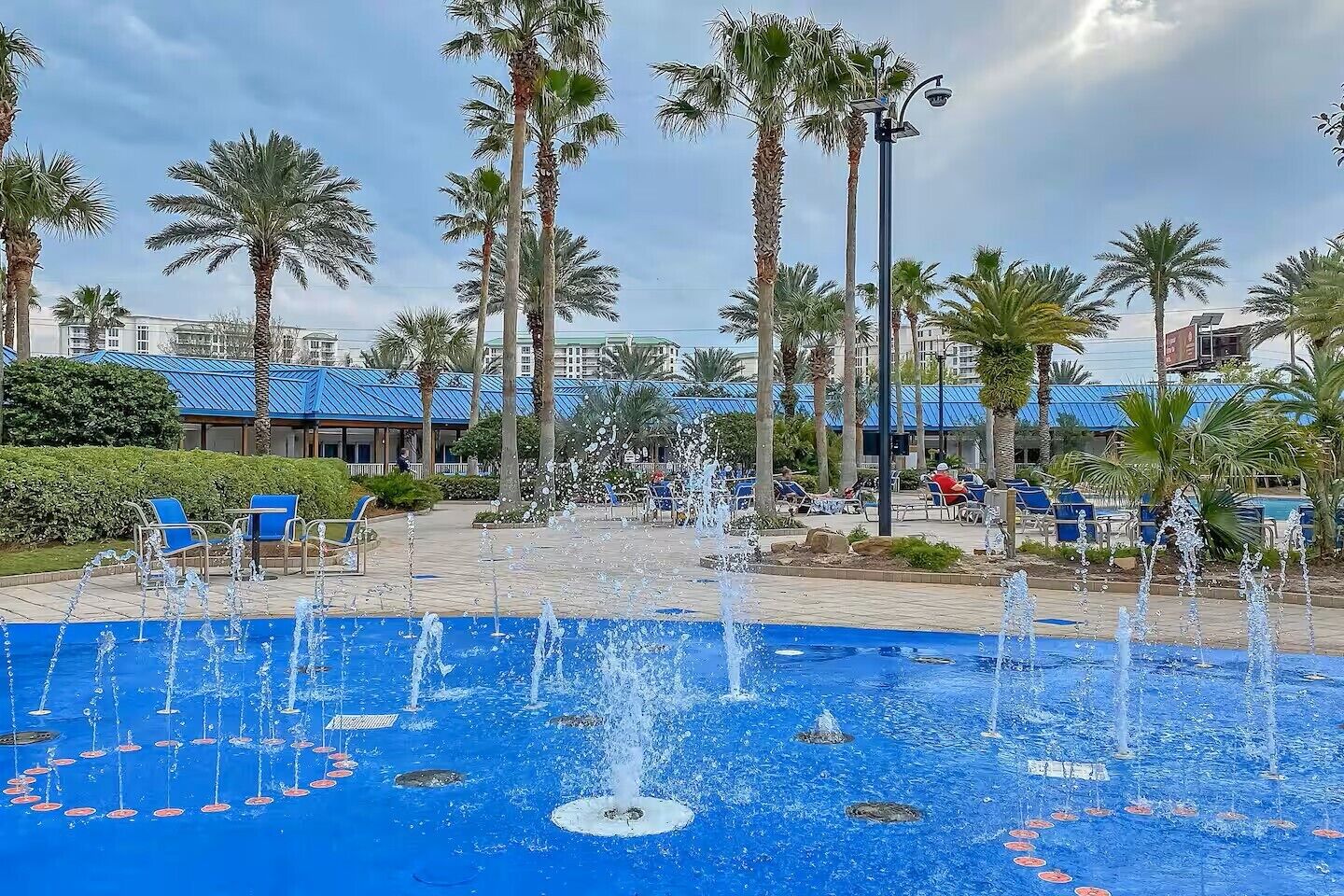 A pool area with multiple fountains, palm trees, and lounge chairs.