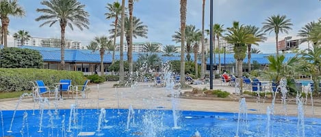 A pool area with multiple fountains, palm trees, and lounge chairs.