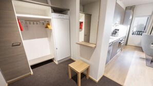 Habitación de hotel compacta con kitchenette, una pequeña mesa de madera y un armario con ropa colgada.