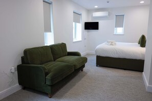 Ein Schlafzimmer mit einem grünen Sofa, einem Bett mit weißer Bettwäsche, einem Flachbildfernseher und einer Klimaanlage.