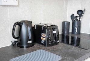 Eine Küchenarbeitsplatte mit Wasserkocher, Toaster und Besteckhalter.