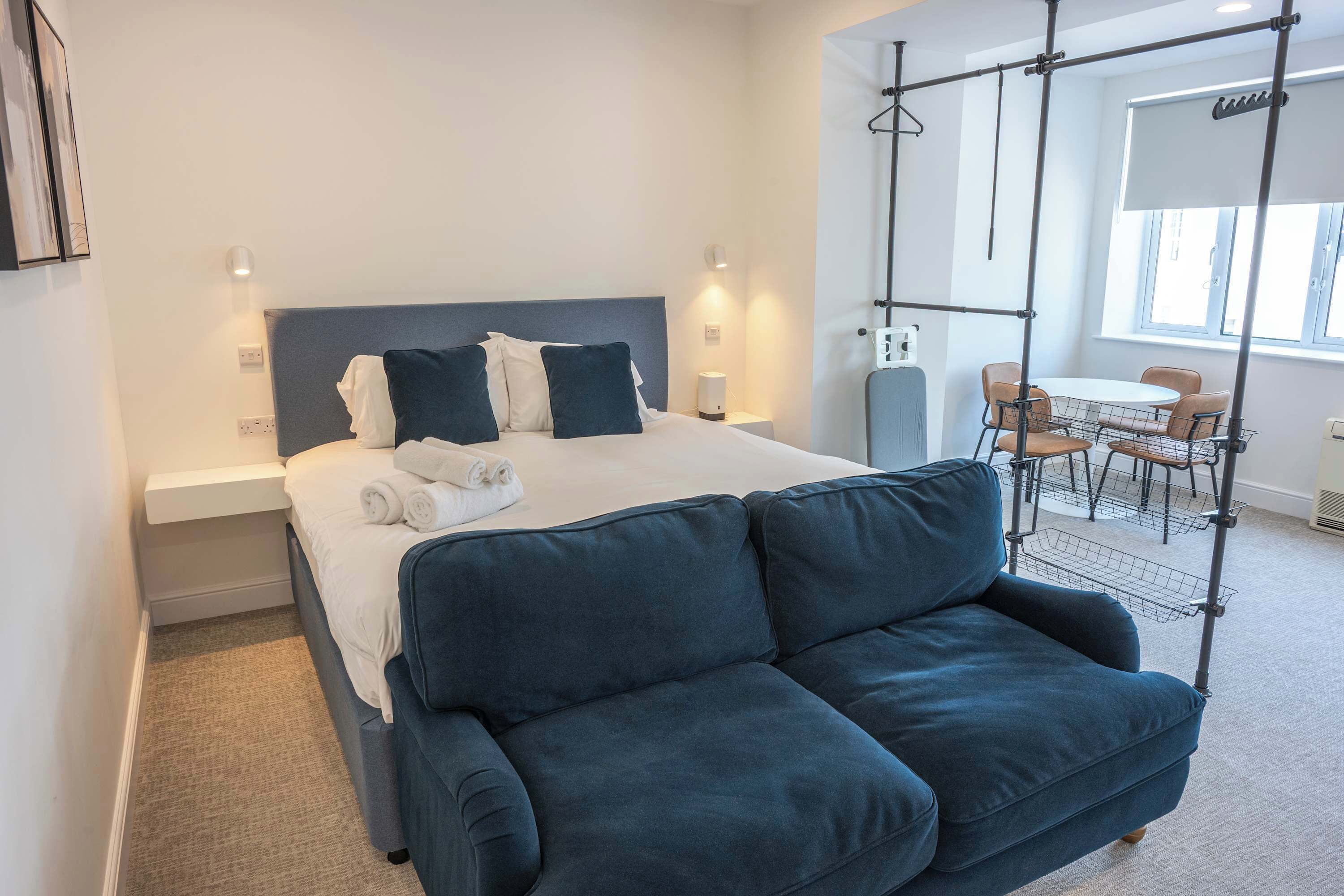 Une chambre d’hôtel moderne avec un lit, un canapé bleu foncé, un bureau avec des chaises et une fenêtre.