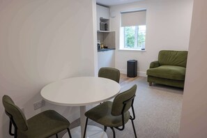 A compact living space with a round table and four chairs, a kitchenette with a microwave, and a green sofa. - The Maycliffe - Studio near Torquay Harbour (Torquay)