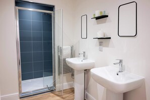 Ein Badezimmer mit Duschkabine aus Glas, zwei Waschbecken und einem Handtuchhalter.