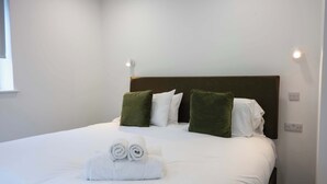 A neatly made bed with white linens and rolled towels, a brown headboard, and green pillows. - The Maycliffe - Studio near Torquay Harbour (Torquay)