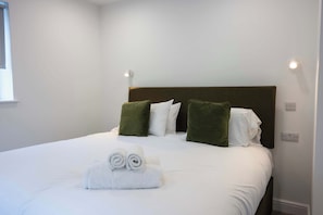 Ein ordentlich bezogenes Bett mit weißen Laken, aufgerollten Handtüchern, einem braunen Kopfteil und grünen Kissen.