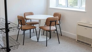 A room with a round table and six chairs, a window with a view, a radiator, and a metal rack. - The Maycliffe - Studio near Torquay Harbour (Torquay)