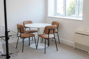 A room with a round table and six chairs, a window with a view, a radiator, and a metal rack.