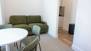 Um quarto com um sofá verde, uma mesa redonda branca e um alto-falante preto.