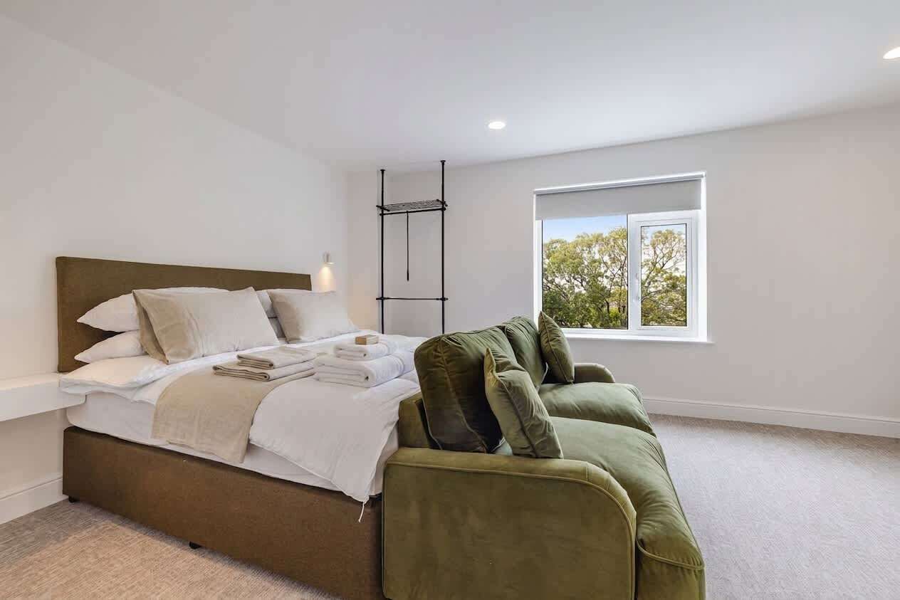 Un dormitorio con una cama, un sofá verde, una ventana y un estante en la pared.