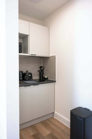 A compact kitchen with white cabinets, a black coffee maker, a toaster, and a black speaker. - The Maycliffe - Spacious Studio near Harbour (Torquay)