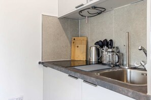 A modern kitchen with a stainless steel sink, a wooden cutting board, and various kitchen appliances. - The Maycliffe - Spacious Studio near Harbour (Torquay)