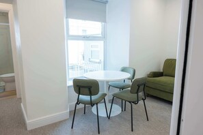 A small, bright room with a round table and four chairs, a green sofa, and a window providing a view of the outside. - The Maycliffe - Spacious Studio near Harbour (Torquay)