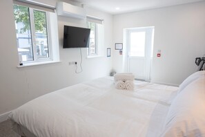 A hotel room with a bed, a flat-screen TV mounted on the wall, a window with a view of the outside, and a door. - The Maycliffe - Modern Studio nr Harbour (Torquay)