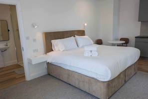 Une chambre d’hôtel moderne avec un grand lit, une table de chevet, une petite table ronde et une salle de bain visible à travers une porte ouverte.