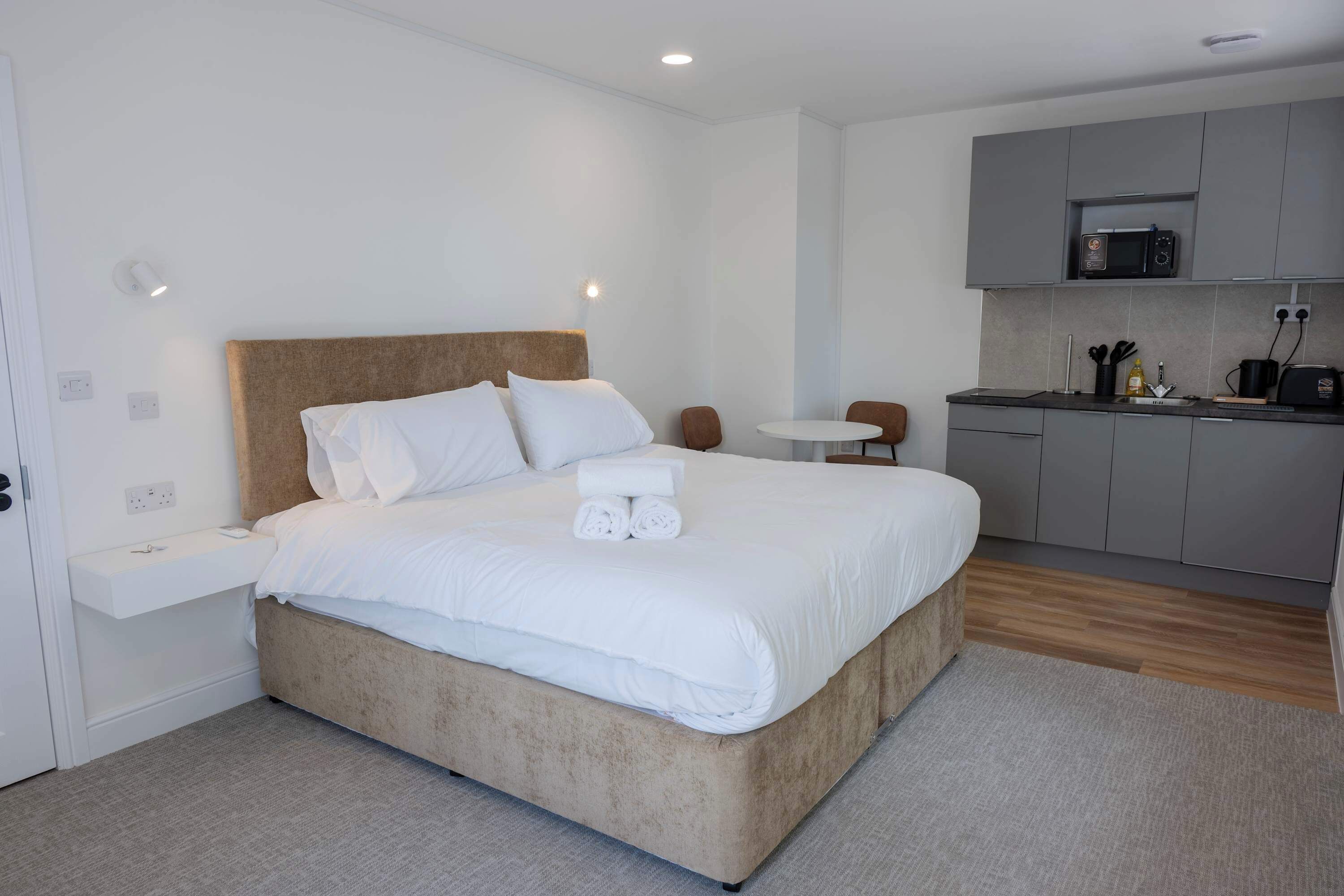 Ein modernes Hotelzimmer mit einem großen Bett, einem kleinen runden Tisch, einer Küchenzeile und einem Badezimmer.