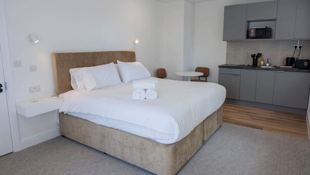 Ein modernes Hotelzimmer mit einem großen Bett, einem kleinen runden Tisch, einer Küchenzeile und einem Badezimmer.