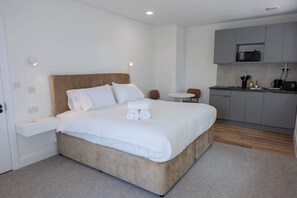 Une chambre d’hôtel moderne avec un grand lit, une petite table ronde, un coin cuisine et une salle de bain.