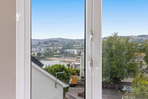 A view through a window of a residential area with a river, buildings, and a truck on the street. - The Maycliffe - Modern Studio nr Harbour (Torquay)