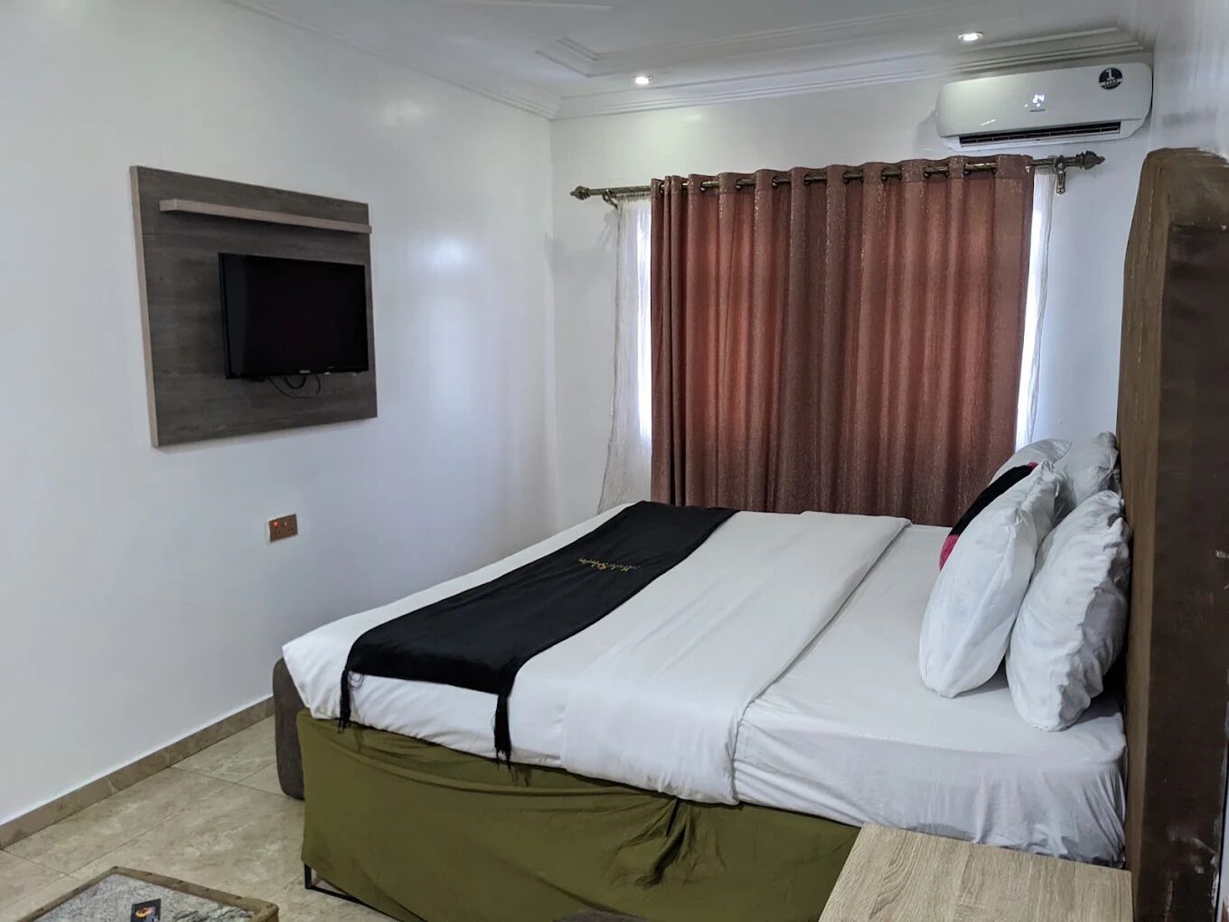 Une chambre d’hôtel équipée d’un lit, d’un téléviseur fixé au mur, d’un appareil de climatisation et d’un rideau.