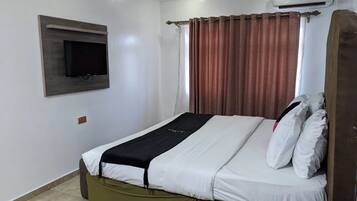Une chambre d’hôtel équipée d’un lit, d’un téléviseur fixé au mur, d’un appareil de climatisation et d’un rideau.