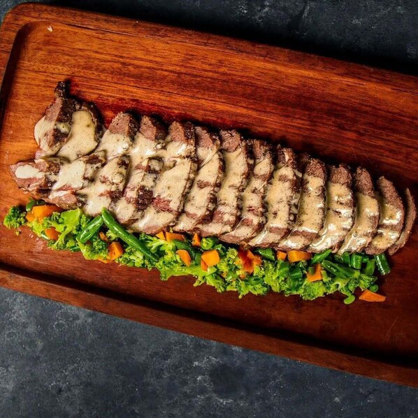A wooden board with sliced meat and a vegetable salad.