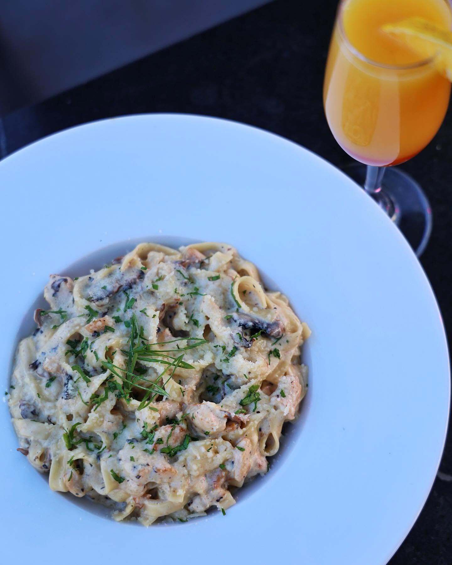 Une assiette de pâtes nappées d’une sauce crémeuse, garnie d’herbes fraîches, et un verre de jus d’orange à côté.