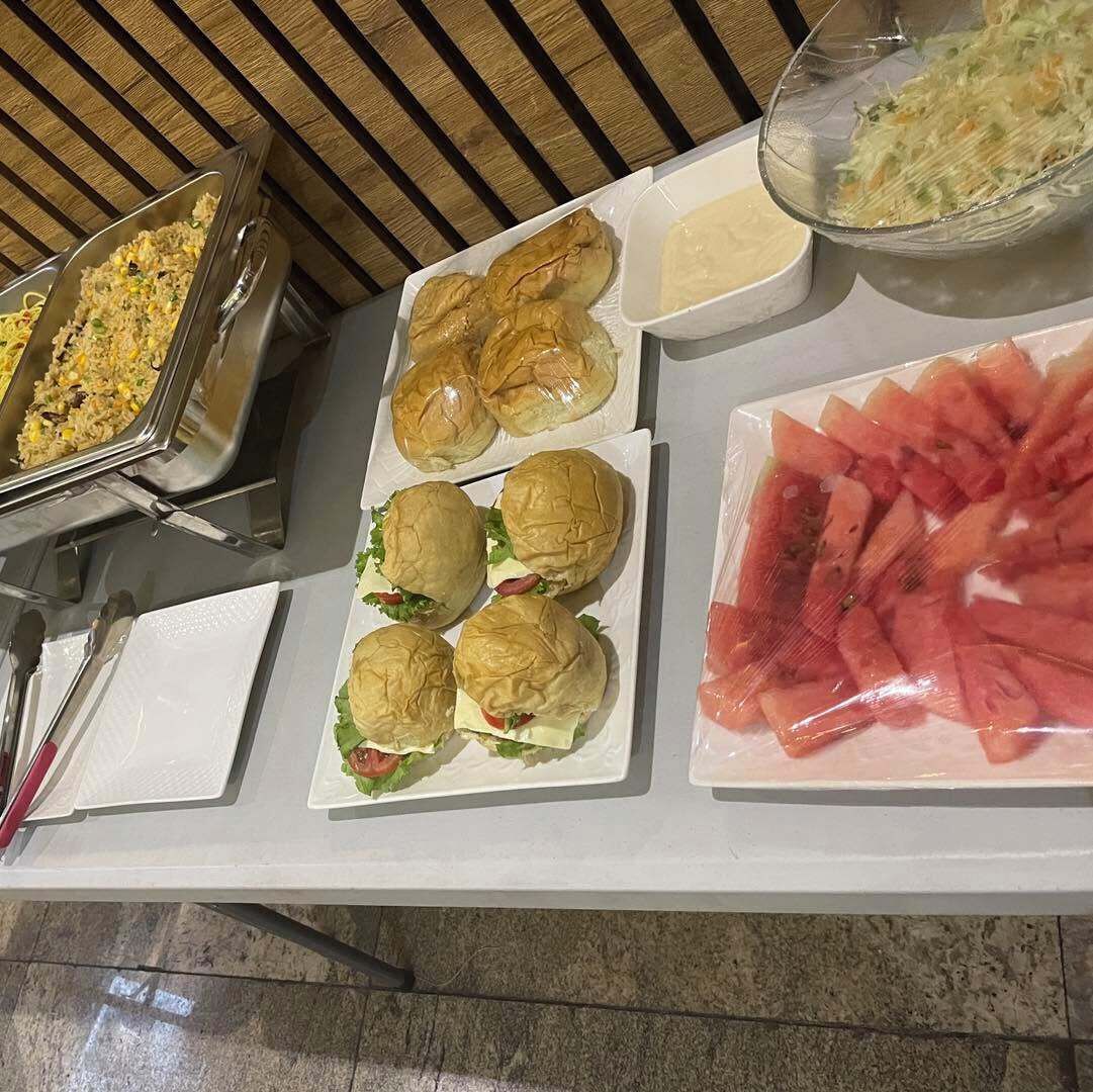 A buffet table with food items including sandwiches, a watermelon salad, and a container of coleslaw.