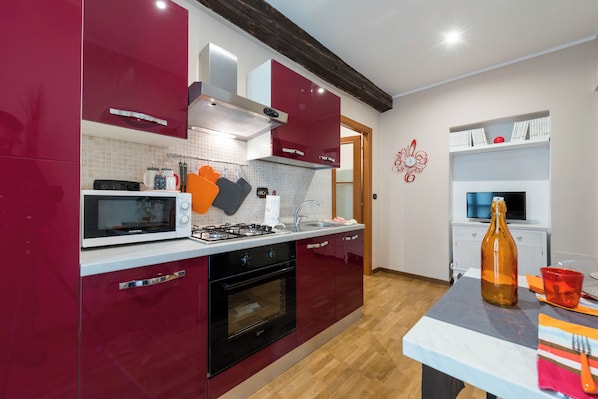 Une cuisine moderne avec des meubles rouges, un four à micro-ondes, une cuisinière et un évier. On y trouve une table avec une bouteille et une tasse.