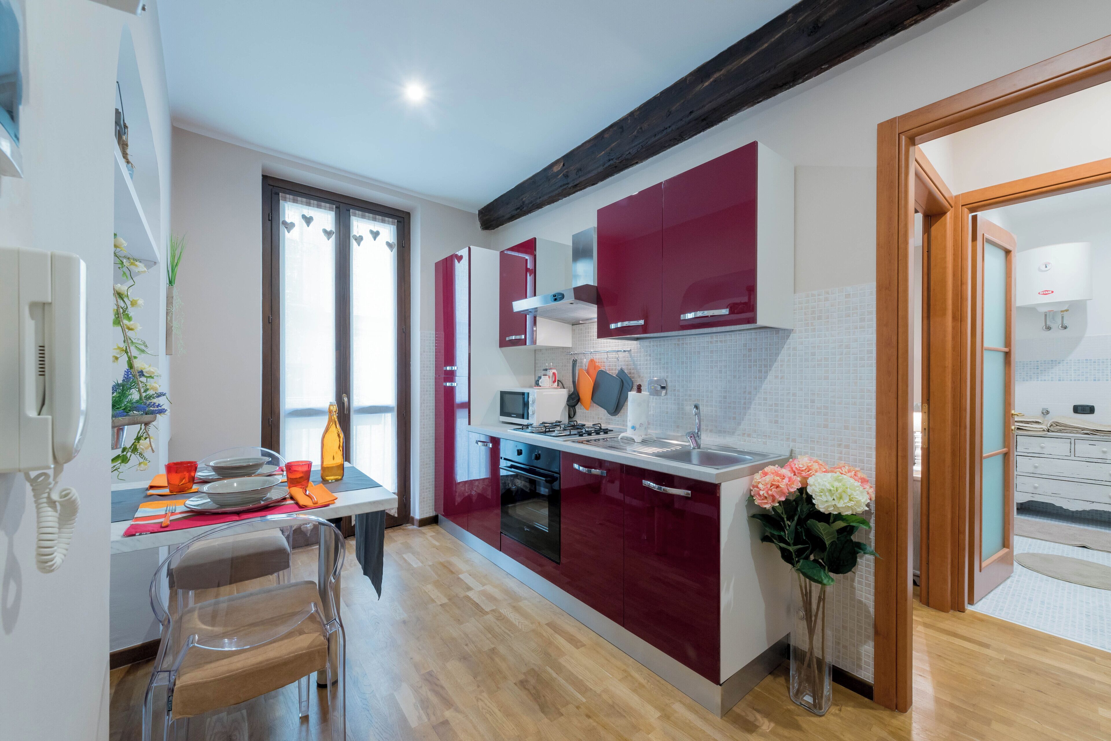 A modern kitchen with red cabinets, a wooden floor, and a dining area with a table and chairs.